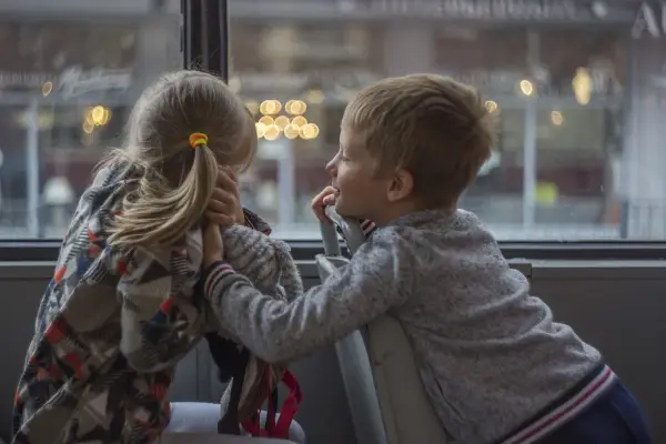 Bambina con disturbo della comunicazione sociale si nasconde, mentre un bambino le parla con un sorriso.